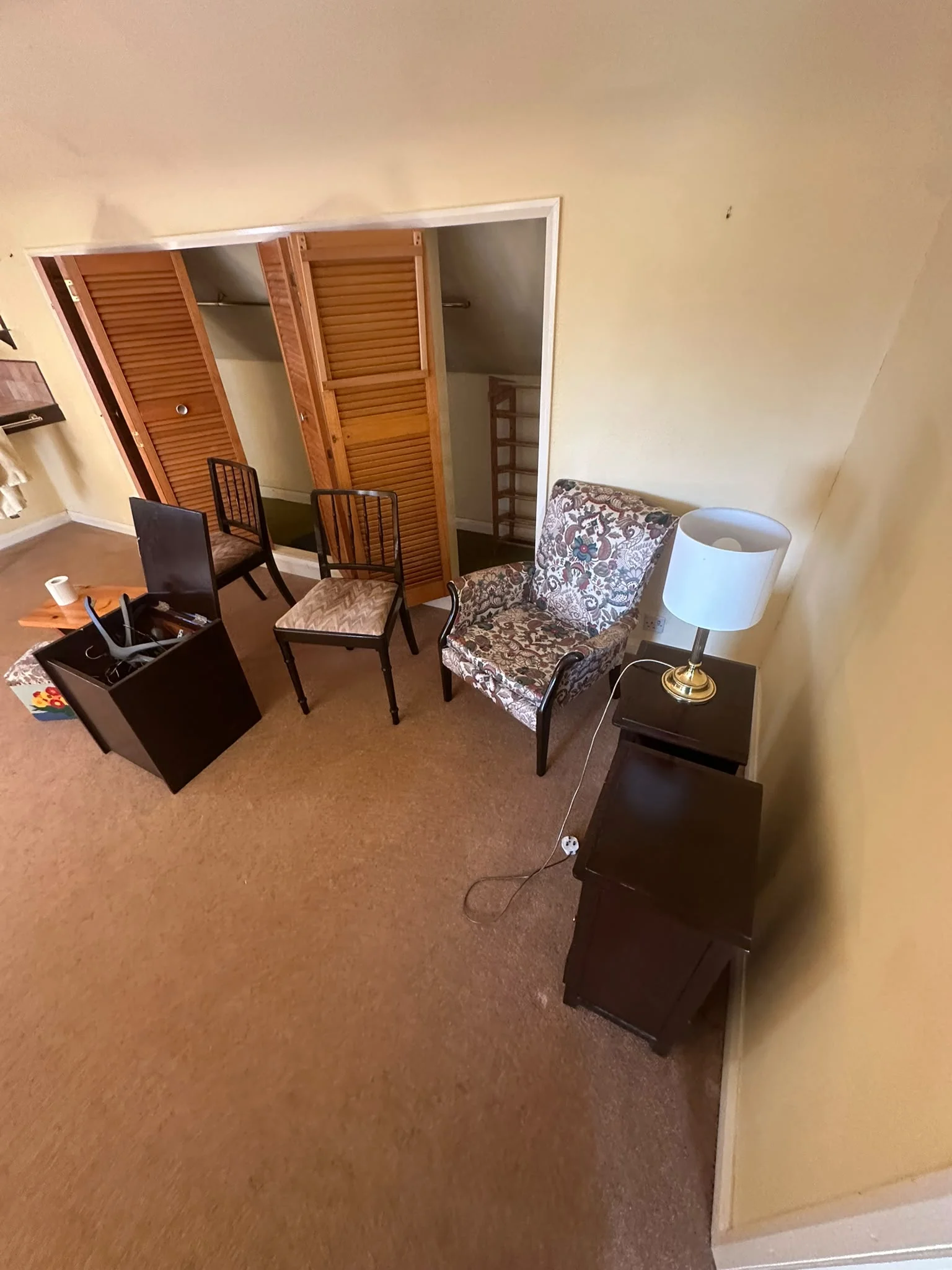 Attic bedroom before clearance with dining chairs, an armchair and a bedside cabinet stacked ready to go