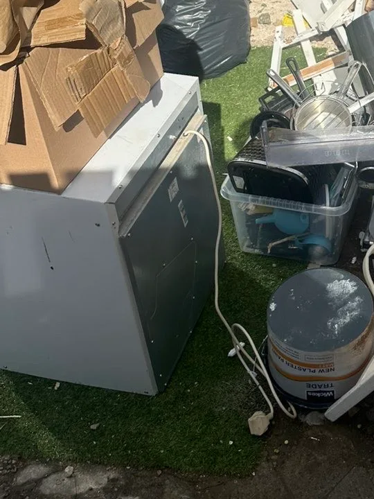 Under-counter fridge with its plug still attached, put out on the grass for collection next to a box of kitchenware and a paint tin